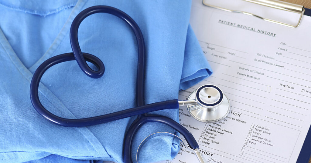 A stethoscope is shaped into a heart. It is lying on blue nurse scrubs and a form.