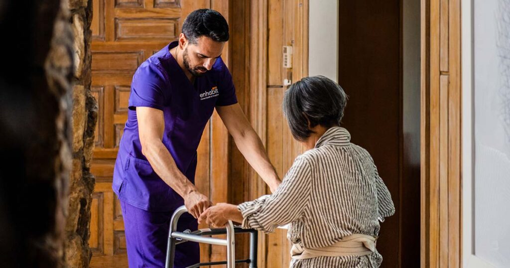 Physical therapist helping home health female patient use a walker around her house